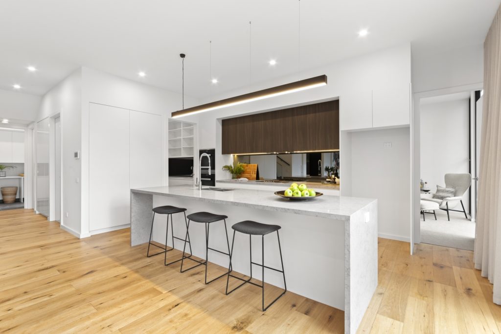Brightly lit, white kitchen with timber floors and downlights.