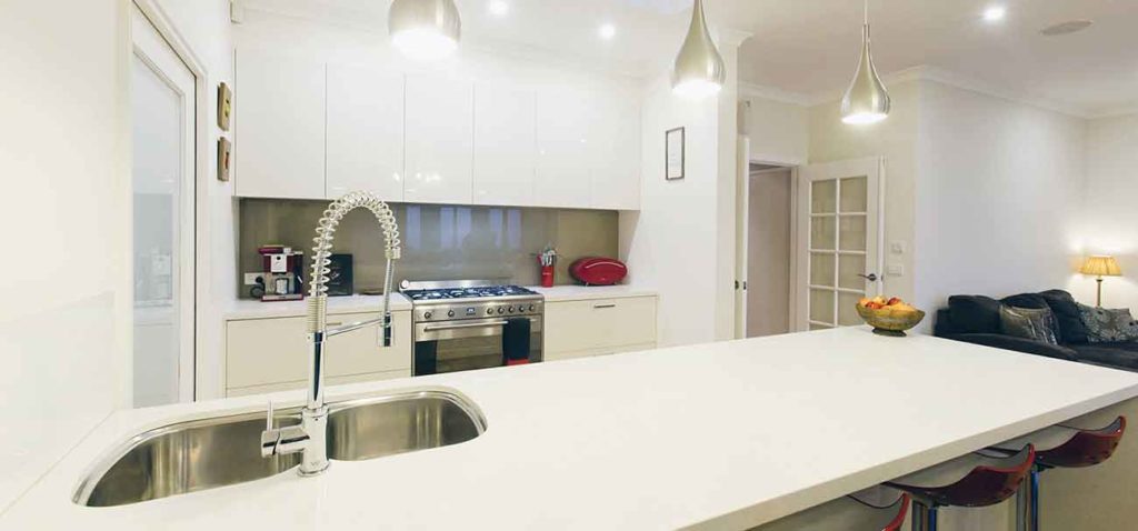Brightly lit white kitchen with hanging lights by Mass Constructions.