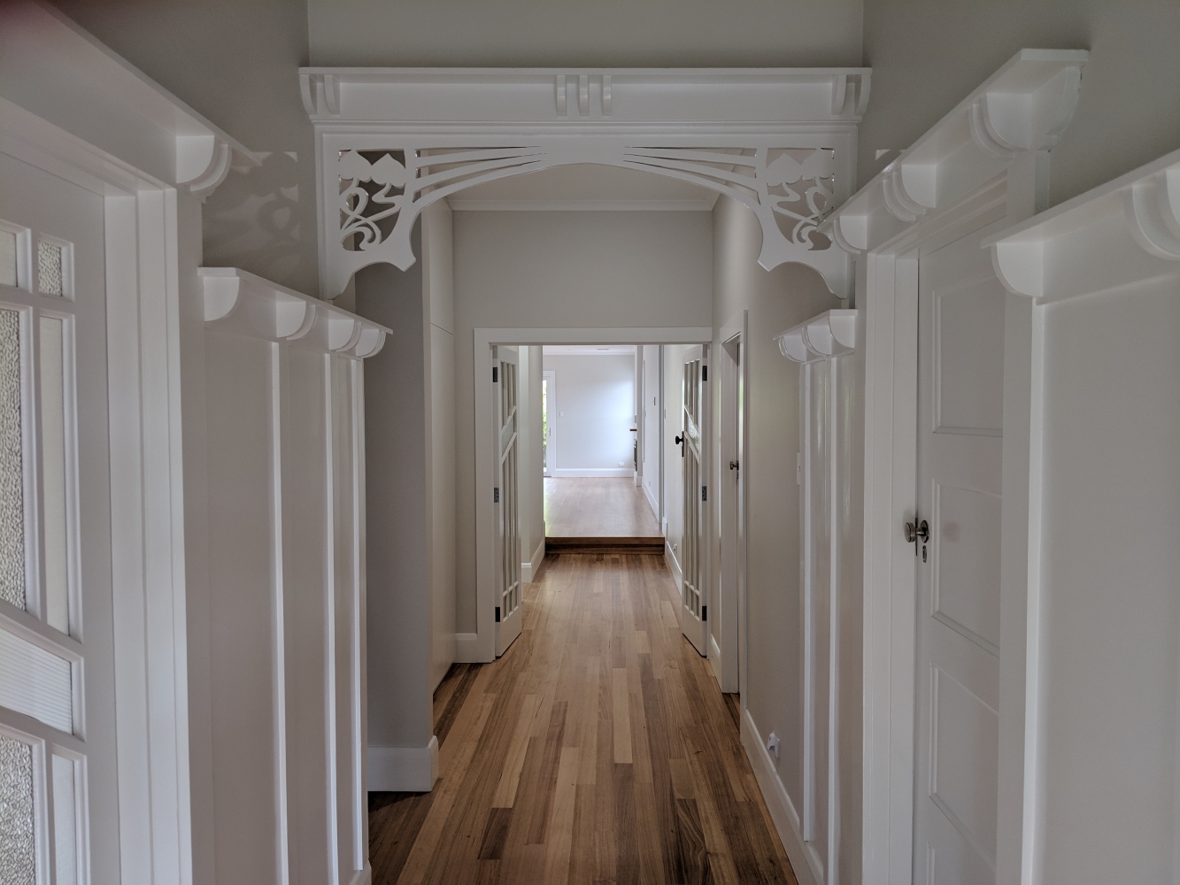 Brightly lit, white hallway with timber flooring by Mass Constructions..