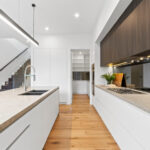 Brightly lit, elegant kitchen with marble top benches, downlights and modern fittings.