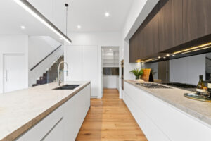 Brightly lit, elegant kitchen with marble top benches, downlights and modern fittings.